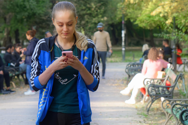 Junge Frau steht in der Stadt und nutzt ihr Smartphone für eine Online-Befragung, Menschen sind im Hintergrund zu sehen.